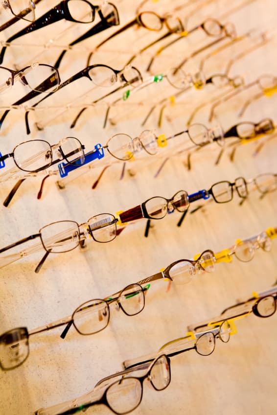 Rows of various eyeglasses on display, each with different frame styles and colours, arranged neatly on a wall-mounted rack.