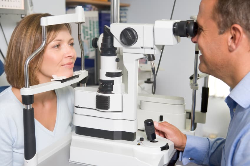 An optometrist examines a patient using a slit lamp in an examination room.